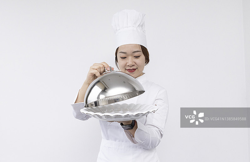 戴着厨师帽、手捧圆顶托盘和空盘子的亚洲女厨师宣传素材图片素材