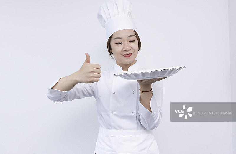 戴着厨师帽、手捧圆顶托盘和空盘子的亚洲女厨师宣传素材图片素材