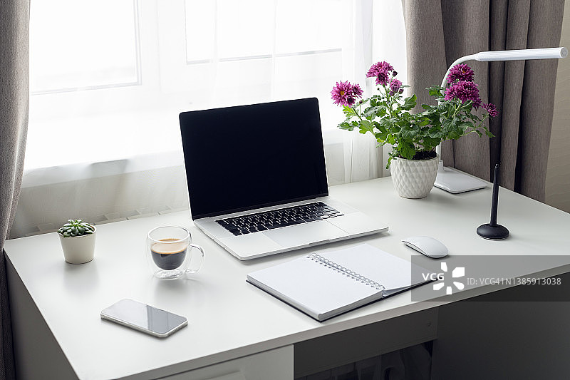 清晨的办公桌，打开的笔记本电脑、咖啡和窗边的鲜花图片素材