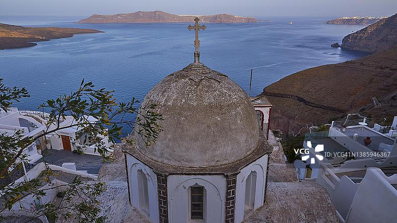 希腊圣托里尼岛的教堂圆顶、房屋、悬崖和锡拉西亚岛清晨广角景色图片素材