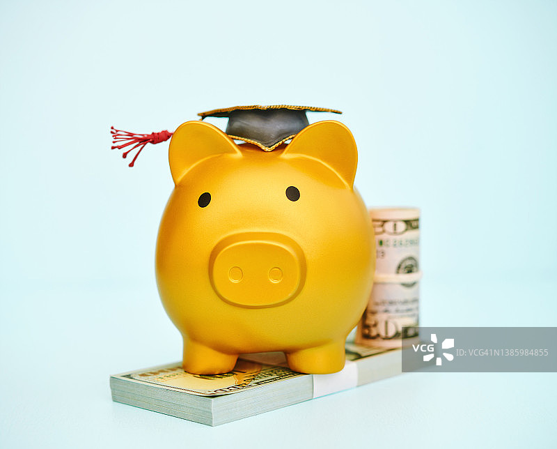 戴着毕业帽的金色小猪存钱罐和美元，教育成本图片素材