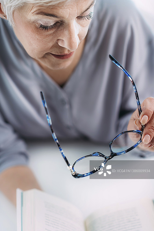 戴眼镜的年长女性努力阅读图片素材