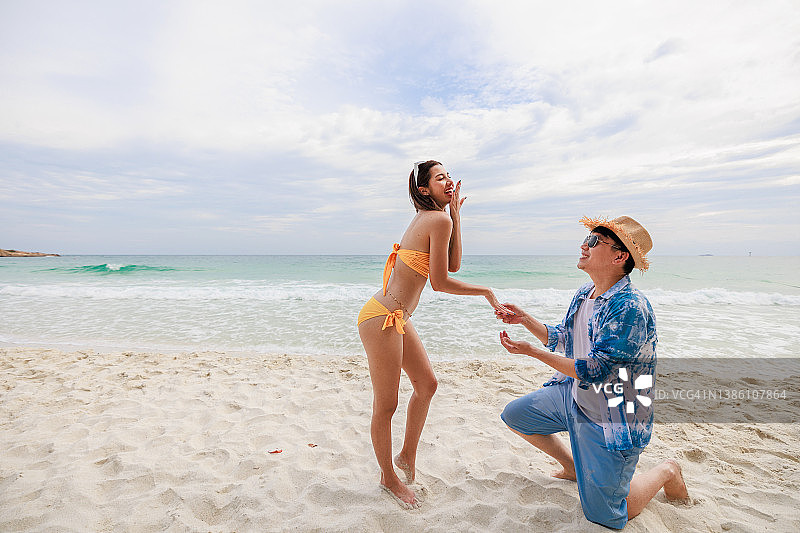 亚洲男人单膝跪在沙滩上向女友求婚图片素材