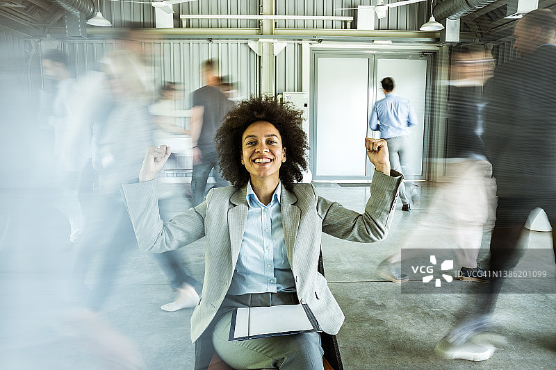 在同事的模糊身影中庆祝成功的快乐女商人图片素材