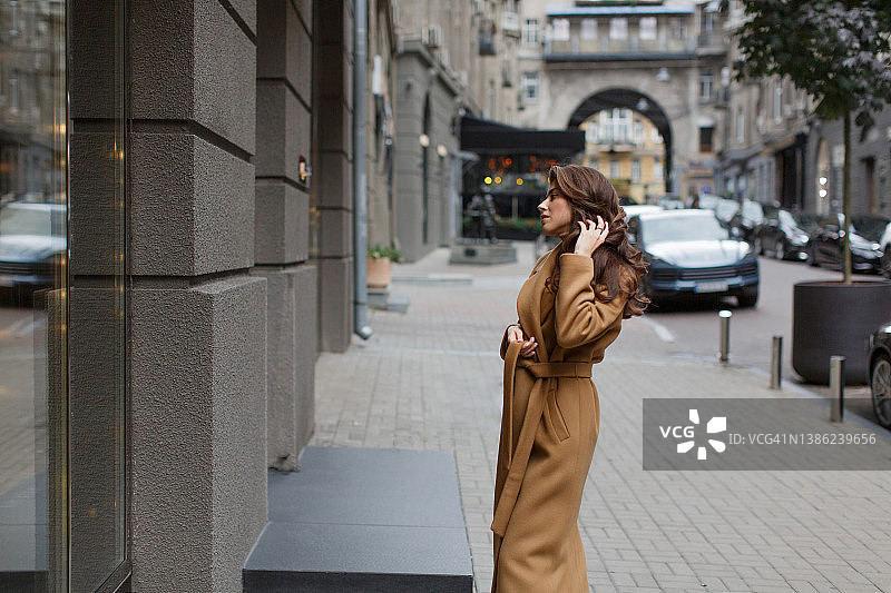 年轻女人身穿浅棕色外套，在窗边欣赏自己图片素材