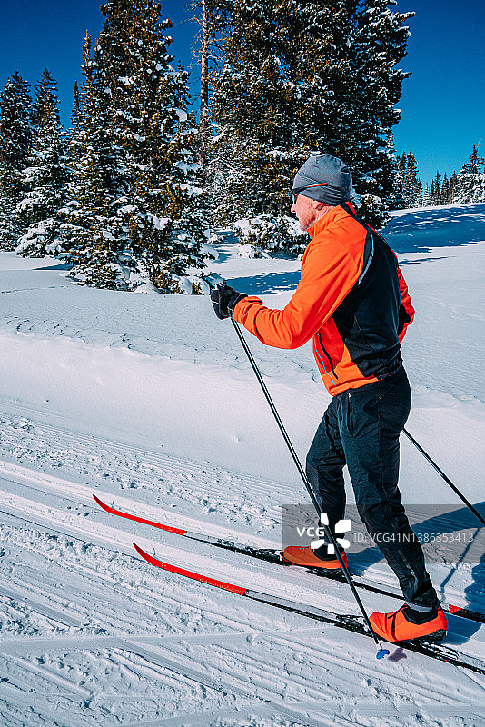 在科罗拉多州晴朗的阳光明媚的日子里，越野滑雪者沿着修整好的小径以对角线大步上坡滑雪图片素材