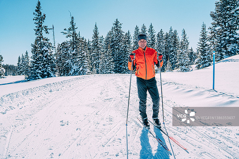 科罗拉多州阳光明媚的晴天里，越野滑雪者手持滑雪杖站在雪道上，面带微笑看向镜头的广角远景图片素材