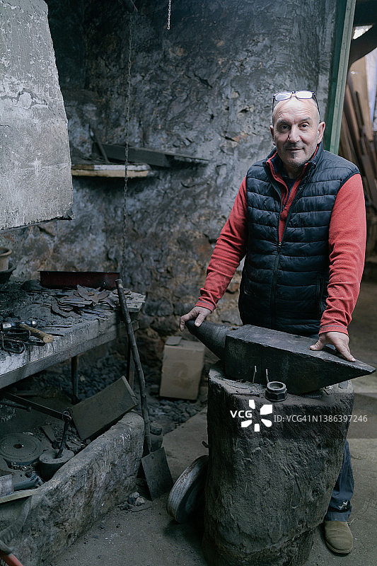 铁匠铺老板在铁砧旁摆姿势看向镜头图片素材