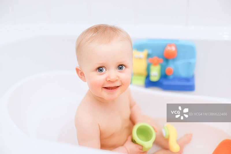 可爱快乐的16个月大的女婴享受她的沐浴时间，周围是一些色彩鲜艳的塑料沐浴玩具图片素材