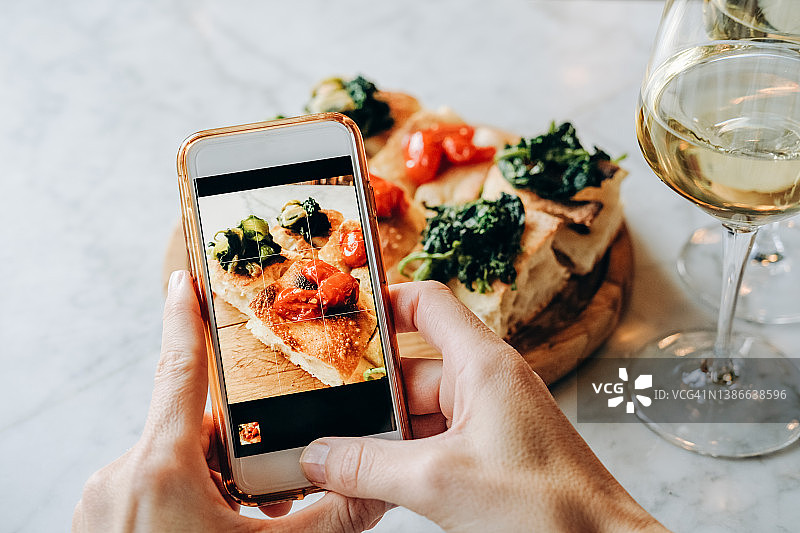 女博主在酒吧用智能手机拍摄食物，意式开胃小吃番茄烤面包和白葡萄酒图片素材