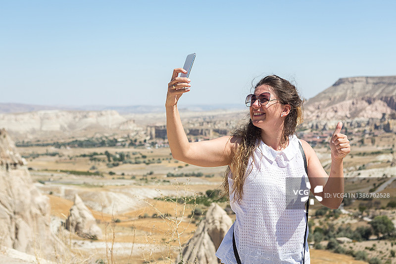 在土耳其卡帕多奇亚的爱之谷附近用智能手机自拍的女人图片素材