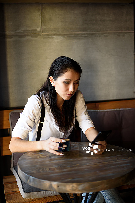 年轻女商人坐在咖啡馆里喝咖啡，用手机图片素材