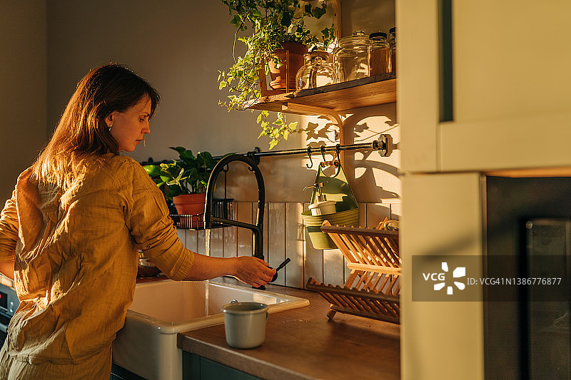 在现代厨房里，女人用清洁液在自来水下清洗煎锅的特写。天然清洁饮食和健康生活方式概念图片素材