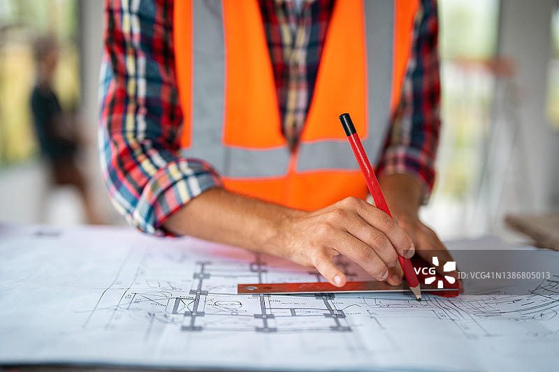 建筑师概念图：工程师在办公室用笔指向桌上的蓝图，复古日落光图片素材