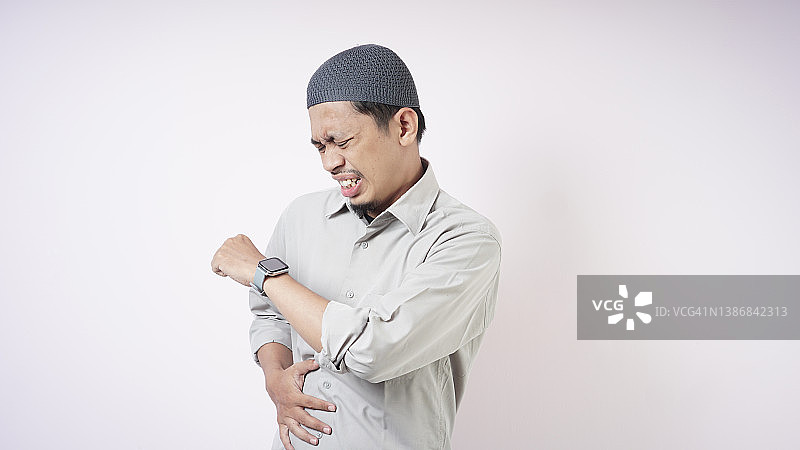 在灰色背景下看智能手表的穆斯林男人图片素材