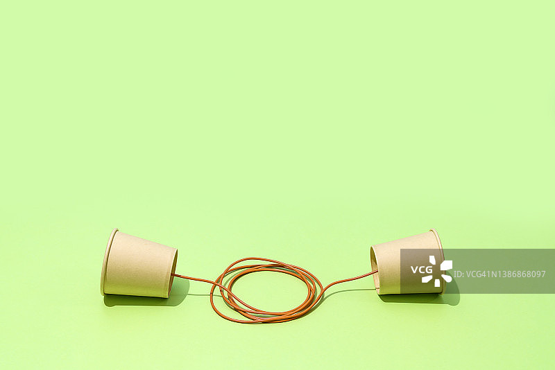 绿色背景上的两个用橘色绳子连接的纸杯图片素材