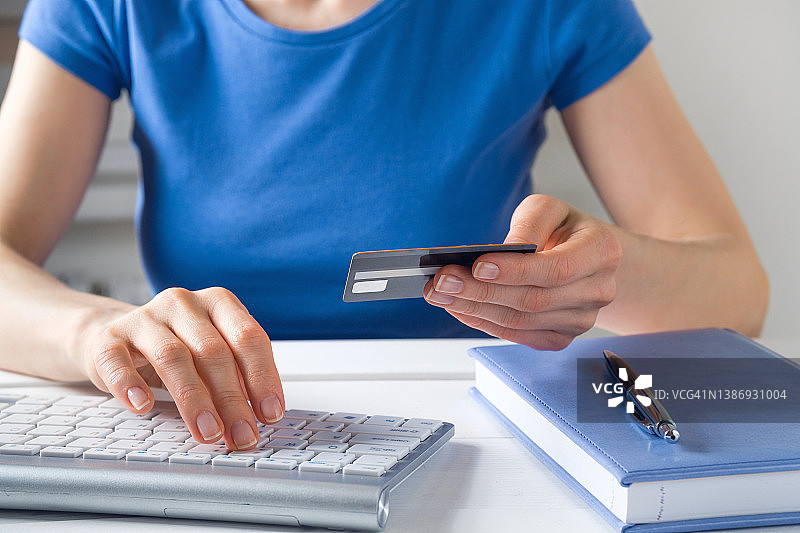 女人拿着信用卡在笔记本电脑键盘上打字，旁边有笔记本和笔，网上购物的概念图片素材