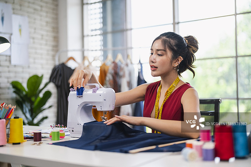 快乐的白人女裁缝在她的工作室里使用缝纫机，自信地笑着，手腕上戴着一个针垫图片素材