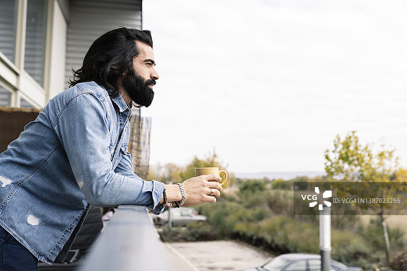 留长发胡子的男人在阳台喝咖啡放松图片素材