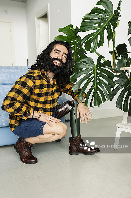 在家中深蹲，微笑看着镜头的截肢并装有假肢的男人图片素材