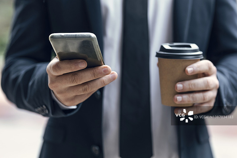 商人拿着咖啡杯用智能手机的手图片素材