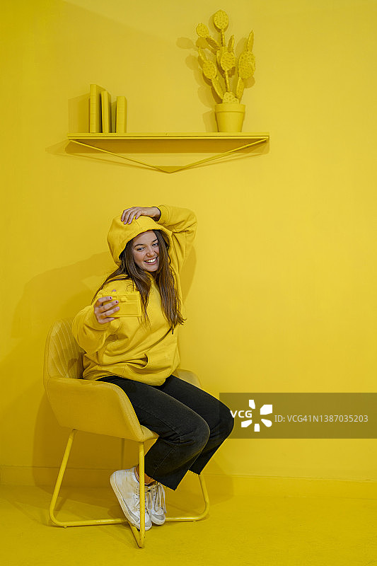 年轻女人在黄色背景前用智能手机自拍图片素材