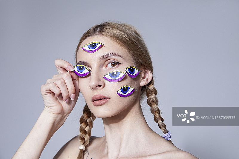 在工作室里脸上贴着眼睛贴纸的辫发年轻女人图片素材