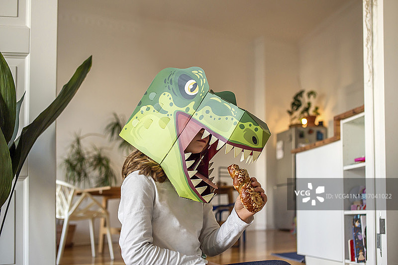 戴着恐龙面具在家吃面包的女孩图片素材