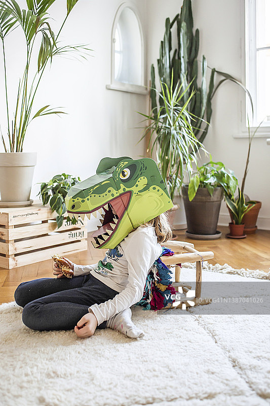 疲惫的女孩戴着恐龙面具坐在家里图片素材