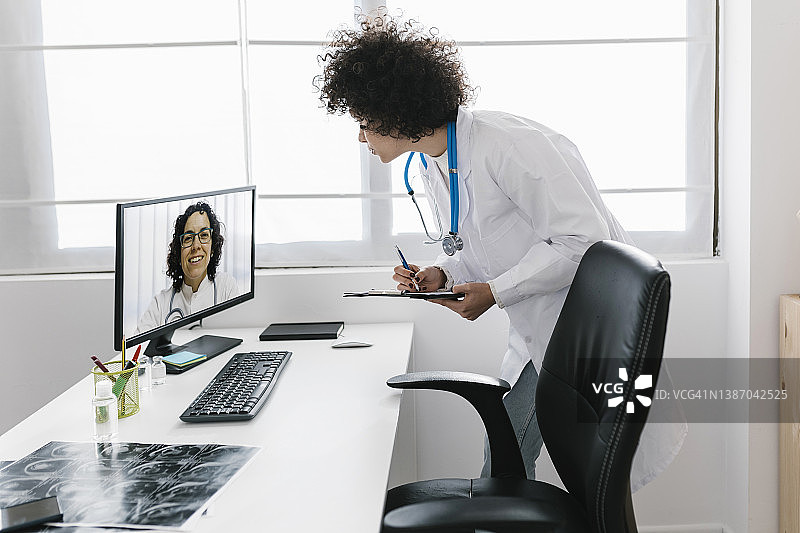 医生在诊所通过台式电脑与同事进行视频通话图片素材