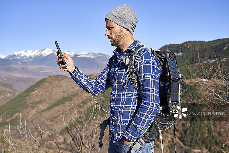 阳光明媚的日子里，男子手插口袋查看智能手机图片素材