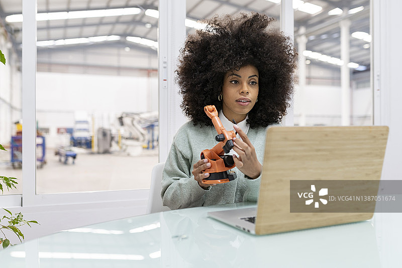 女商人通过笔记本电脑视频通话展示工厂中的机械臂模型图片素材