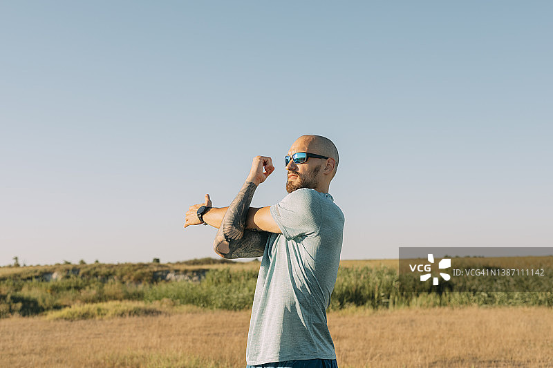 在阳光明媚的一天，高加索跑步者在田野里伸展身体图片素材