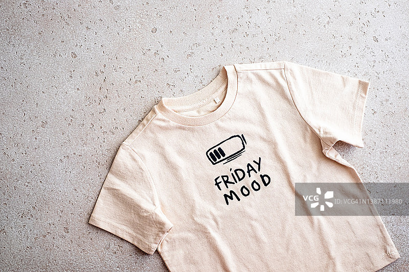 浅色背景上印有“Friday mood”的米色T恤特写，俯视图片素材