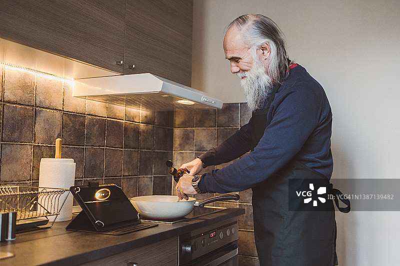 一位留着长胡子的中年男人通过数位板观看烹饪教程图片素材