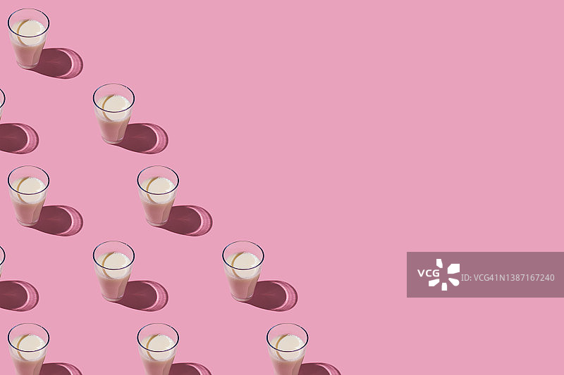 粉色背景下左侧装满牛奶的玻璃杯图案：乳制品、短缺、钙、成长和饮用概念图片素材
