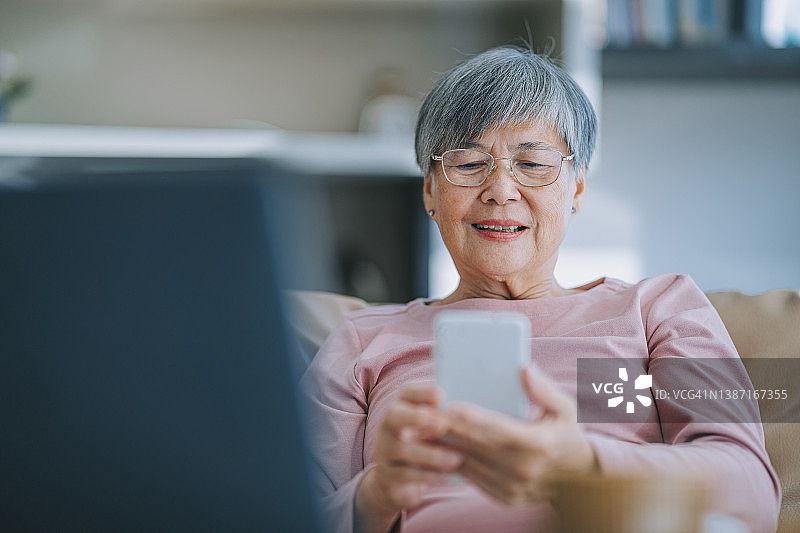 中国老年妇女在城市公寓的客厅里用智能手机阅读短信图片素材