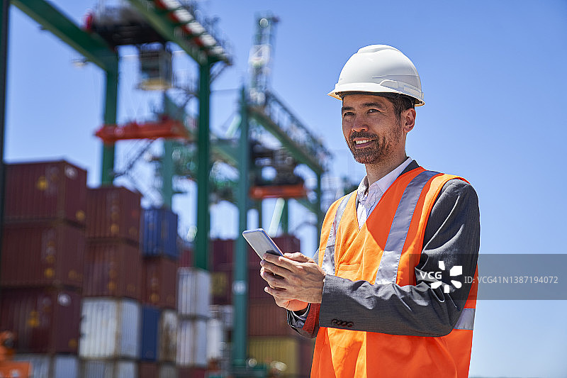 站在货运集装箱堆场的亚裔美国男工程师正在使用智能手机图片素材
