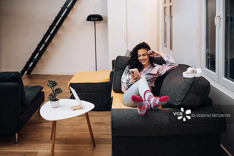 在客厅沙发上使用手机的年轻女子，现代白色内饰图片素材