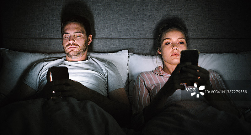 年轻情侣在家中躺在床上使用智能手机图片素材