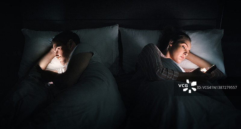 年轻情侣在家中躺在床上使用智能手机图片素材