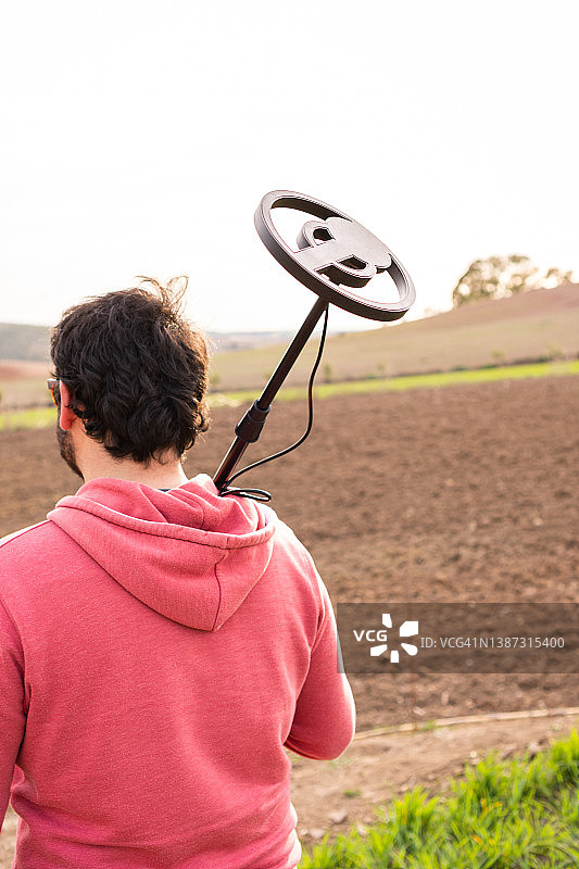 在乡村日落时携带金属探测器的年轻人（面部不可辨认）图片素材