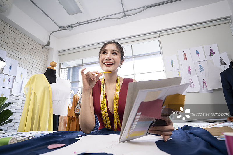 亚洲女设计师在工作室的桌子上思考并在纸上为顾客订单绘制草图图片素材
