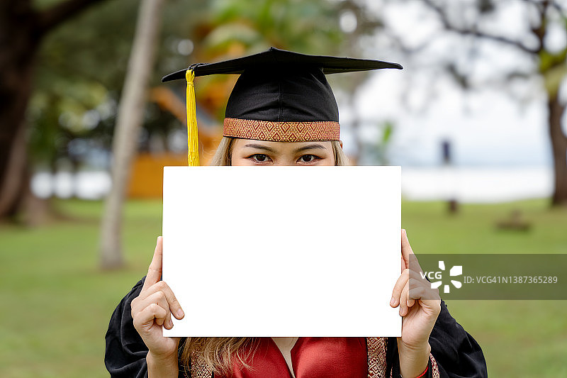 年轻女人戴着毕业帽和毕业袍，拿着白色标语牌图片素材