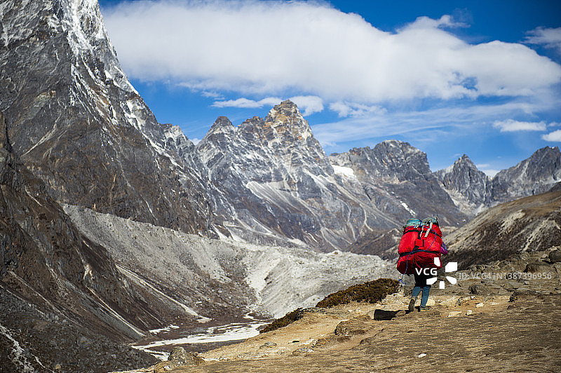 夏尔巴搬运工背着旅行行李袋徒步前往尼泊尔索卢昆布丁波切村，背景是喜马拉雅山峰图片素材