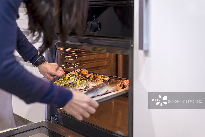 女人从烤箱里取出美味的海鲈鱼图片素材