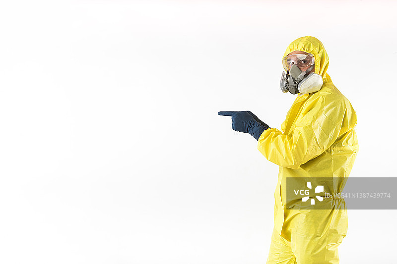 身穿黄色核防护服、戴着面罩和防护眼镜的技术员用手指指向一侧，背景为白色。核能与疫情概念图片素材