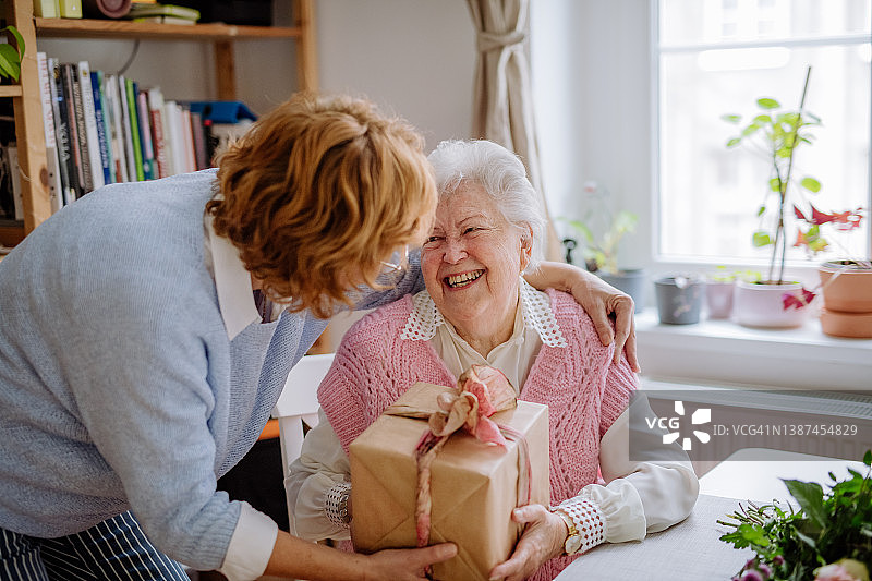 快乐的老年母亲在家收到成年女儿的礼物，母亲节概念图片素材