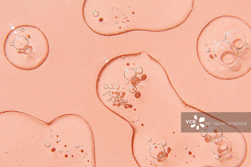 粉色背景上的透明精华液滴，透明质酸凝胶液体，平铺俯视图片素材