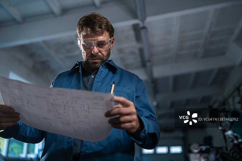 在金属车间里拿着蓝图的中年产业工人图片素材